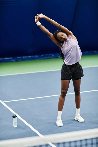屋内コートでのテニスの試合の準備中にストレッチ若い黒のスポーツ女性の完全な長さの肖像画 — ストック写真