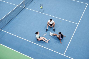 Kapalı tenis kortunda rahatlayan ve grafik mavisi döşeme üzerinde oturan bir grup insanın minimum üst görünümü, kopyalama alanı