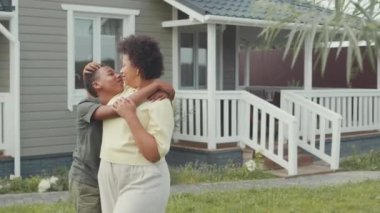 Afro-Amerikan kadının orta boy portresi ve sevgili 12 yaşındaki oğlu yazın evlerinin önünde kameraya poz veriyorlar.