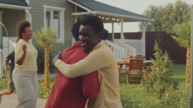 İki neşeli Afro-Amerikan çiftin yaz mevsiminde çocuklar için evin bahçesinde buluşup birbirlerini mutlulukla kucakladıkları orta boy bir fotoğraf.