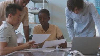 Profesyonel erkek ve kadın mühendislerden oluşan çok ırklı genç bir ekip el ele verip, masa başında oturan güneş panelleri projesini tartışacaklar.