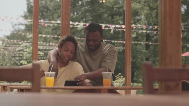 카페에서 테이블에 앉아있는 스마트 폰에서 스포츠 게임을보고 아들과 아프리카계 미국인 — 비디오