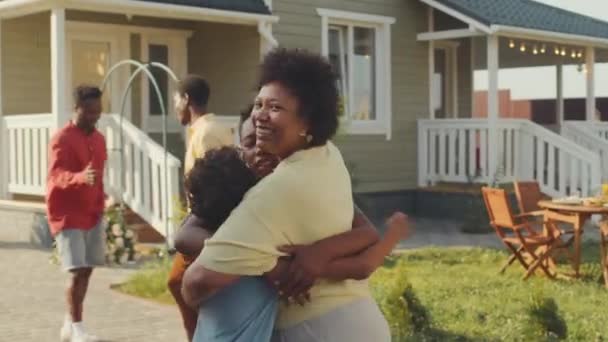 外の庭の緑の芝生で家族の夕食のために一緒に取得しながら 彼女の十代の甥を迎え 抱擁する陽気な黒人女性のミディアムショット — ストック動画