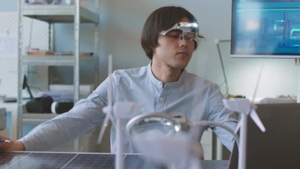 年轻的亚洲男性工程师 头带放大镜检查太阳能电池板并将数据输入膝上型计算机 同时开展办公室可持续性项目 — 图库视频影像