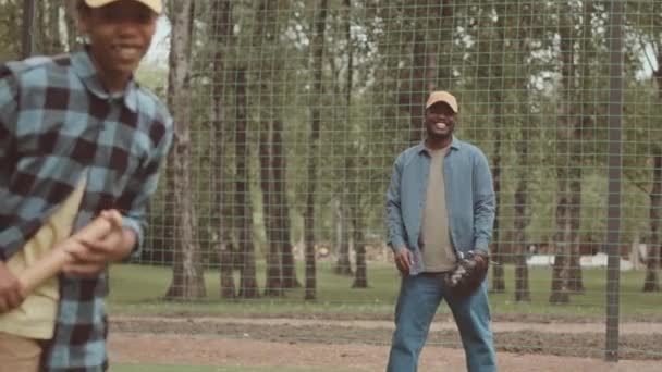 アフリカ系アメリカ人の父親と12歳の息子が夏に公園で野球を練習する中程度のスローモ — ストック動画