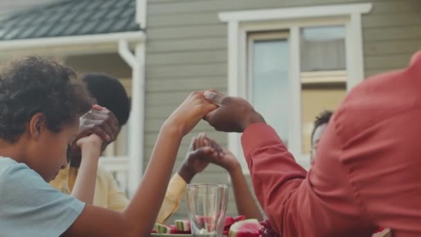 アフリカ系アメリカ人の家族が手を握り 夏の裏庭で一緒に昼食を食べながら祈るのを待つ — ストック動画