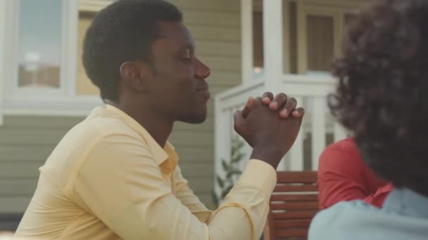 晴れた日の裏庭で友人や家族とランチをしながら祈っている若い黒人の男を待つ — ストック動画