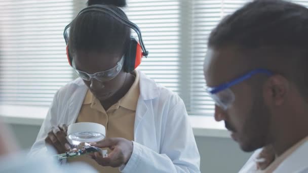African American Female Computer Engineer Lab Coat Examining Part Motherboard — Stock Video