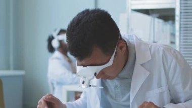 Asian scientist engineer in headband magnifier and lab coat examining motherboard while doing research in laboratory