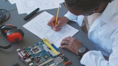 Male computer engineer in lab coat drawing scheme of motherboard while working alone at factory