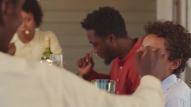 Waist up of big friendly African American family dining together on porch of their house on warm summer evening