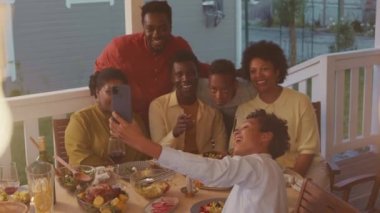 Big African American family taking selfie portrait on smartphone during dinner on porch of their house on warm summer evening
