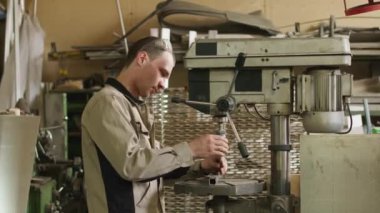 Medium shot of young mechanic man in uniform working with machine tool at factory