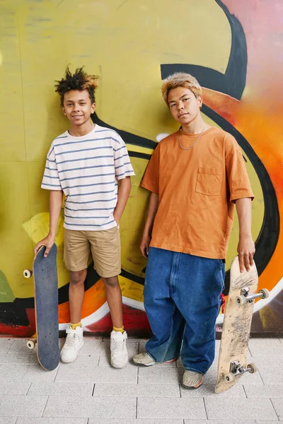 Pionowy Portret Dwóch Nastolatków Deskorolkami Stojących Pod Zieloną Ścianą Graffiti — Zdjęcie stockowe