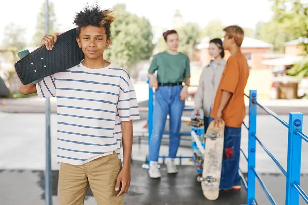 バックグラウンドで友人のカメラの多様なグループを見ているスケートボードと微笑む10代の男の子の肖像画 コピースペース — ストック写真