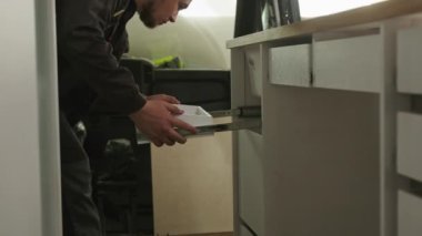 Bearded man working at factory assembling white kitchen set in camper automobile