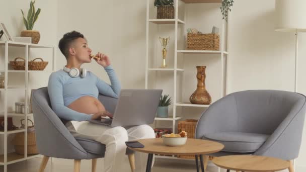 Contemporary Young Pregnant Woman Using Laptop Eating Waffles Sitting Armchair — Wideo stockowe