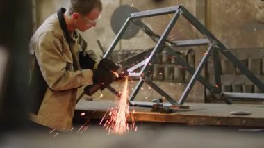 Medium shot of professional angle grinder in protective glasses metalworking in workshop