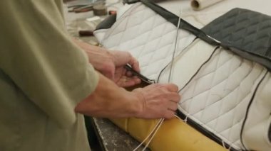 Cropped shot of unrecognizable worker sewing details to each other while making leather car seat cover at factory