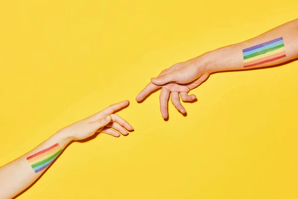 Vibrant shot of two hands reaching out with LGBT flags on yellow background Creation style