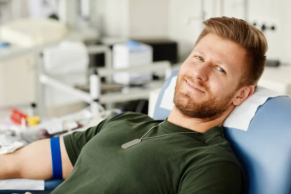 照片上的士兵躺在献血中心的椅子上 看着相机 微笑着献血 — 图库照片