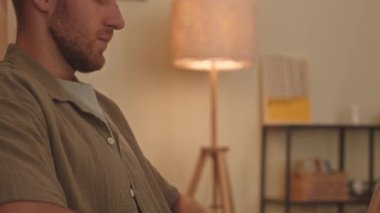 Tilt up shot of young Caucasian man vaping while working on laptop at night from home office