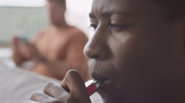 Close up of young Black man vaping indoors in office, exhaling thick steam