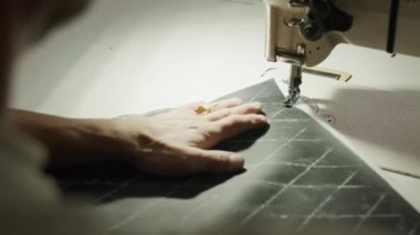 Unrecognizable factory worker making black leather car seat covers on sewing machine in workshop