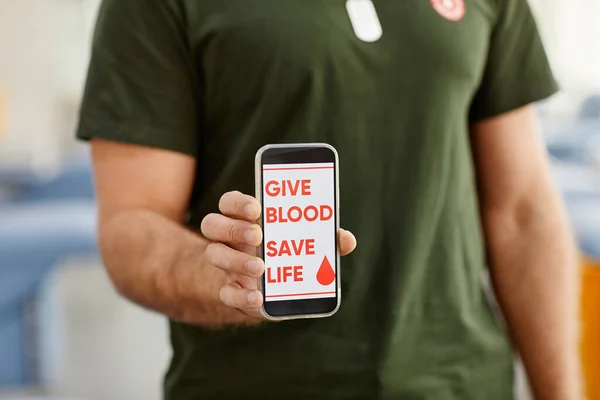 献血センターでスマートフォンを保持している男性のクローズアップ救命スローガン コピースペース — ストック写真