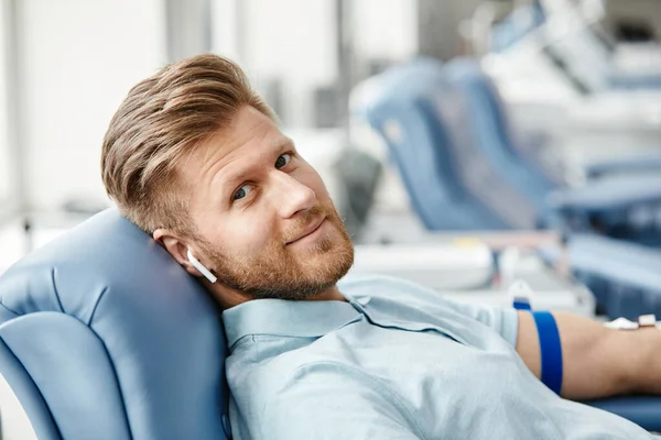 照片上的年轻人微笑着献血 躺在医疗中心舒适的椅子上 看着相机 — 图库照片