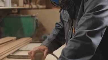 Profesyonel erkek katılımcının güvenlik maskesi ve kulaklıklar takıp atölyedeki ahşap kalasları elektrikli odun cilasıyla parlatmasını çek.