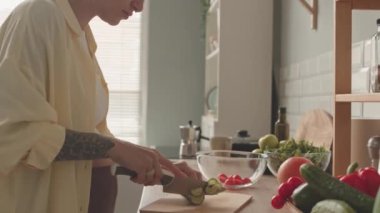 Tilt up shot of modern pregnant woman with arm tattoo and short haircut making healthy vegetable salad at kitchen