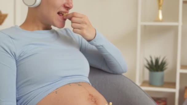 Smiling Young Pregnant Woman Eating Sweets While Watching Comedy Film — Stockvideo