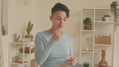 Medium shot of modern young short haired pregnant woman taking prenatal supplements at home