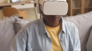Medium closeup of concentrated African American girl in vr headset playing vr games at home using controller