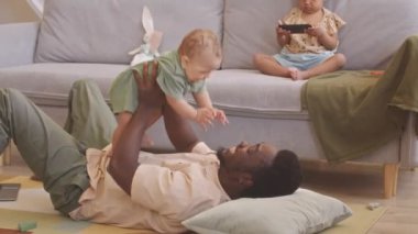 Genç siyah adam, oturma odasında sırtüstü uzanmış, küçük tatlı oğlunu havaya fırlatırken, büyük kızı da kanepede akıllı telefondan çizgi film seyrediyordu.