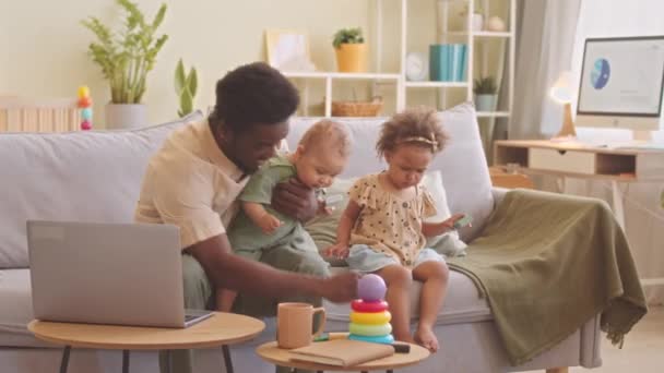 ハッピー アフリカ系アメリカ人のお父さん 人の幼児の子供は ビット混乱ながら居心地の良いリビングルームでソファーで一緒に遊んで — ストック動画