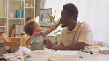 Neşeli genç Afro-Amerikalı adam ve küçük kızı evde birlikte eğleniyor suluboya resimlerle birbirlerinin yüzlerini acıtıyorlar.