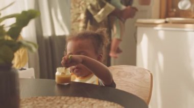Güzel bir Afrikalı Amerikalı bebek mutfak masasında bebek püresi yerken babası küçük kardeşini besliyor.