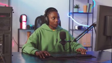 Evde bilgisayar oyunu oynarken mikrofonla oyuncularla konuşan konsantre olmuş Afrikalı Amerikalı kız belini kaldır.