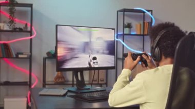 Çift ırklı bir gencin evdeki bilgisayarda FPS oyunu oynarken kontrolör kullanırken çekilmiş arka plan görüntüsü.
