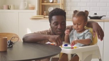 Afrikalı Amerikalı baba ve küçük kız mutfakta pastel boyalarla resim çiziyorlar.