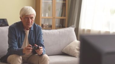 Orta karar beyaz adamın video oyunu oynarken görüntüsü oturma odasındaki koltukta oturan kontrolörle.