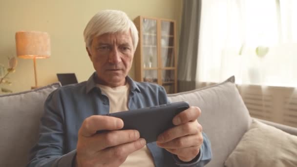 Disparo Mano Anciano Emocionado Jugando Juego Teléfono Inteligente Sentado Sofá — Vídeo de stock