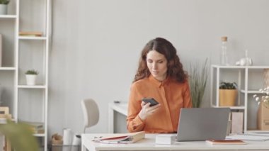 Çağdaş minimalist ofiste çalışırken cep telefonuyla konuşan genç beyaz iş kadını.
