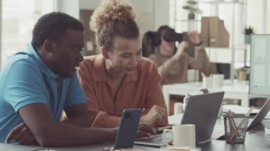 Laptop ekranına bakarken projeyi tartışan birkaç genç iş arkadaşı ve meslektaşları modern bilişim ofisinde arka planda sanal gerçeklik yaşıyorlar.