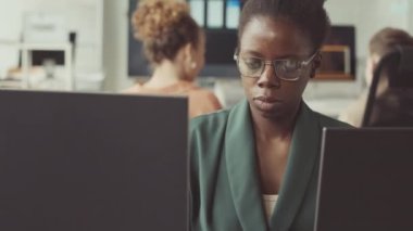 Genç Afrikalı Amerikalı kadın programcının parlak modern ofiste bilgisayar üzerinde çalışmasını destekleyin.