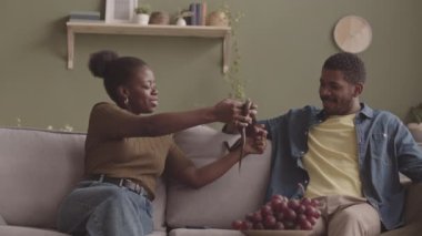 Zeytin yeşili duvarlı oturma odasında evcil yılanlı kanepede oturan ve bir sürü çiçekli genç Afro-Amerikan çifti.