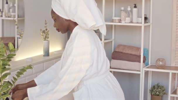 穿着白色浴衣 头戴毛巾的非洲裔年轻女性在豪华浴室的镜子前做日常护肤时 使用棉垫的速度中等 — 图库视频影像