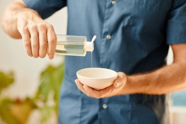 SPA kulübünde oturuma hazırlanan seramik kaseye masaj yağı döken adama yaklaş, boşluğu kopyala.